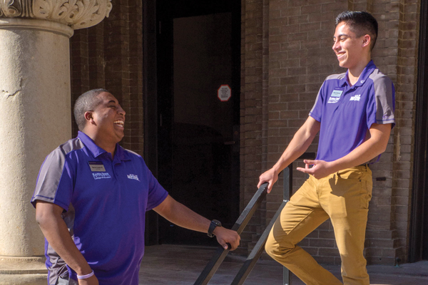 two male African American students stand talking on campus building steps